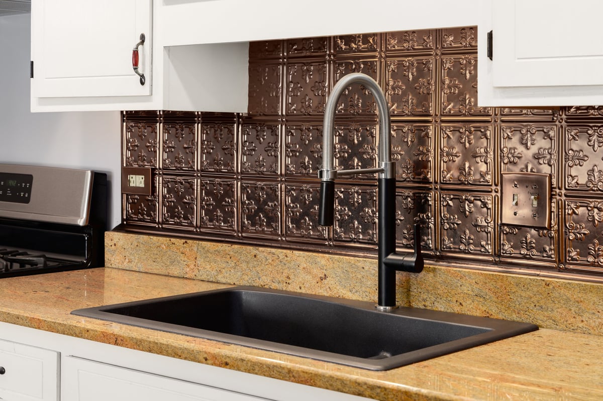 White vanity cabinets with a black ceramic sink and copper backsplash