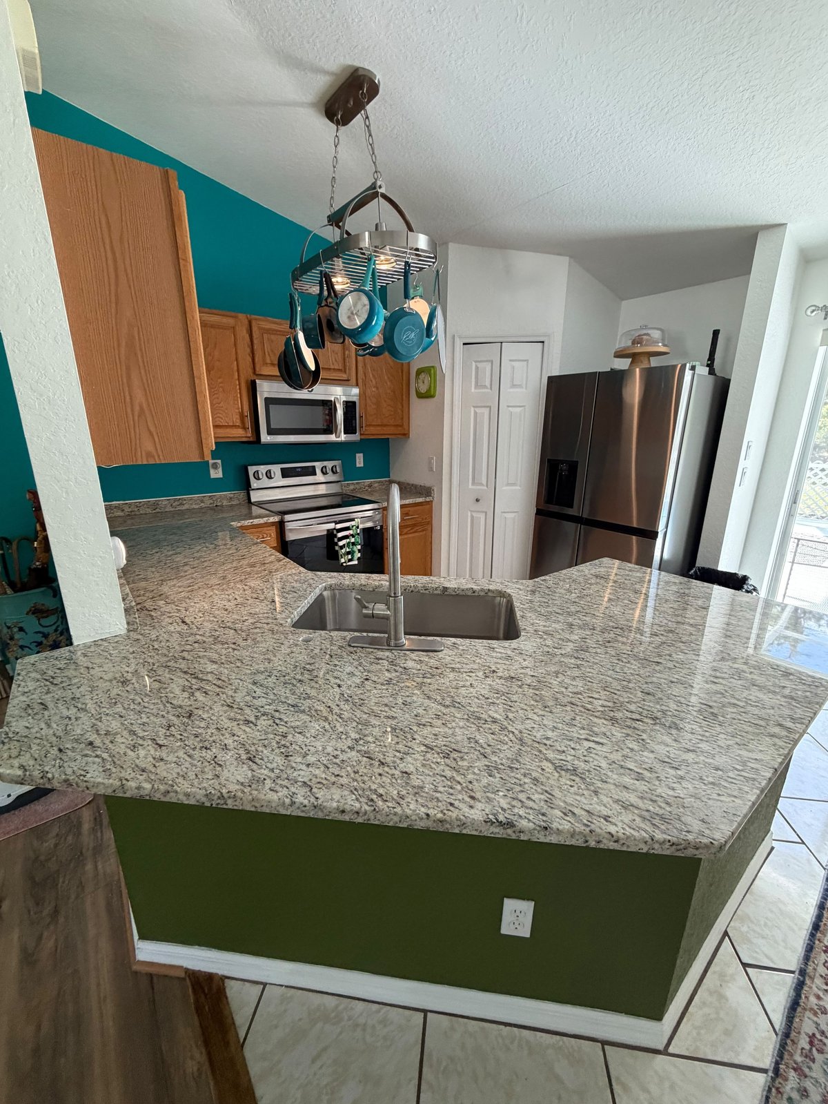 Modern kitchen with granite island, wood cabinets, turquoise accent wall, and stainless steel appliances