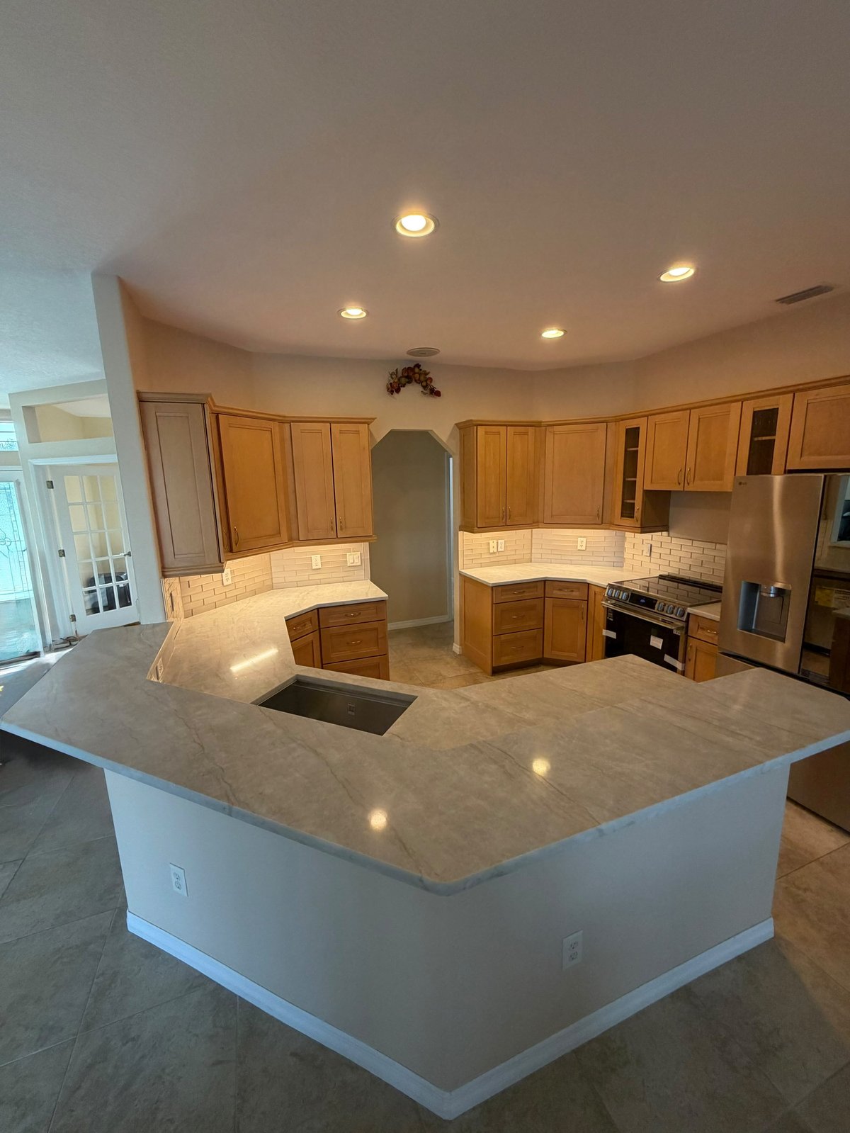 Large modern kitchen with curved island, wooden cabinetry, granite countertops, and recessed ceiling lights