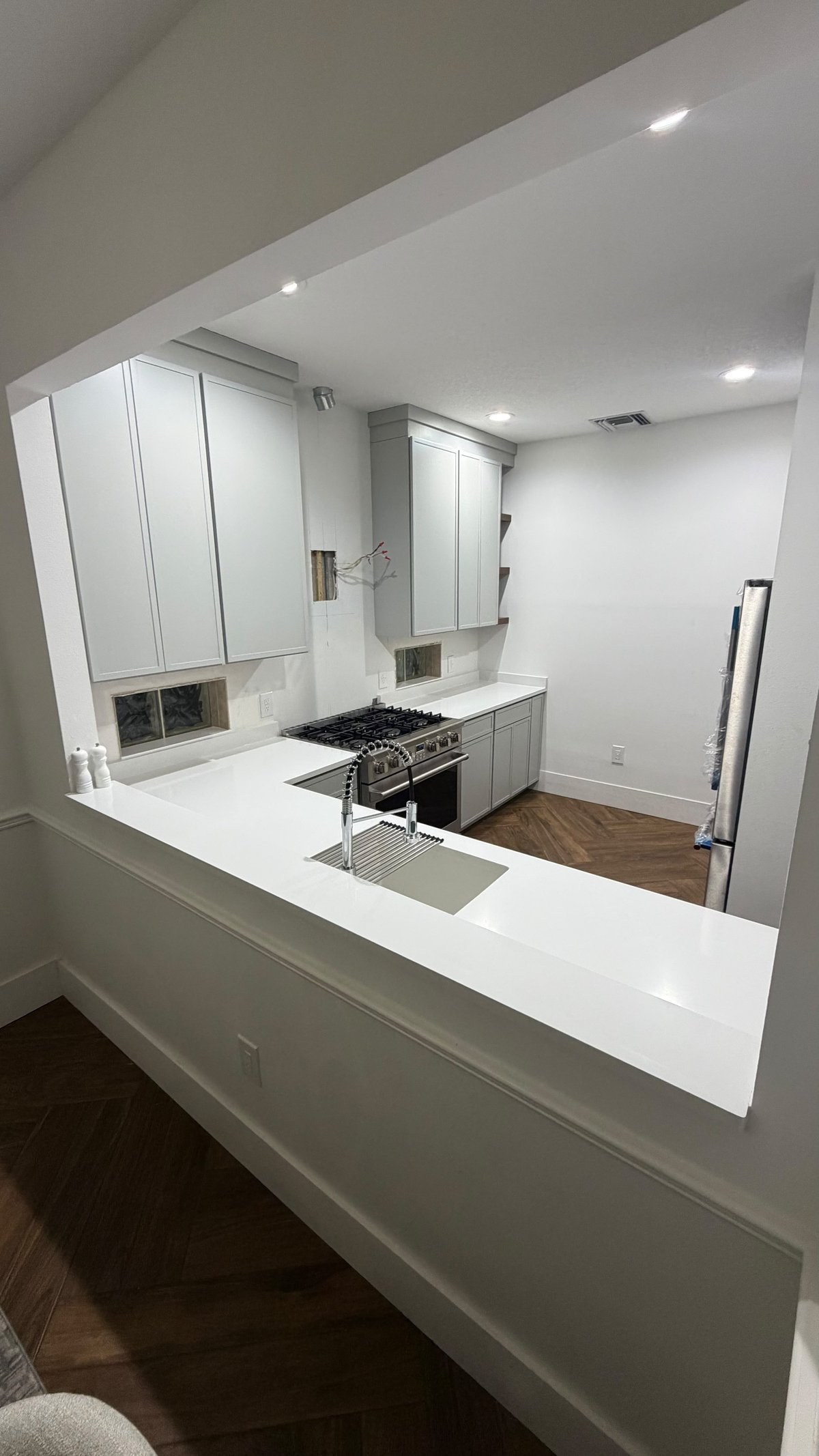 Modern kitchen with white cabinetry, black gas stove, white countertops, and recessed lighting viewed through an opening