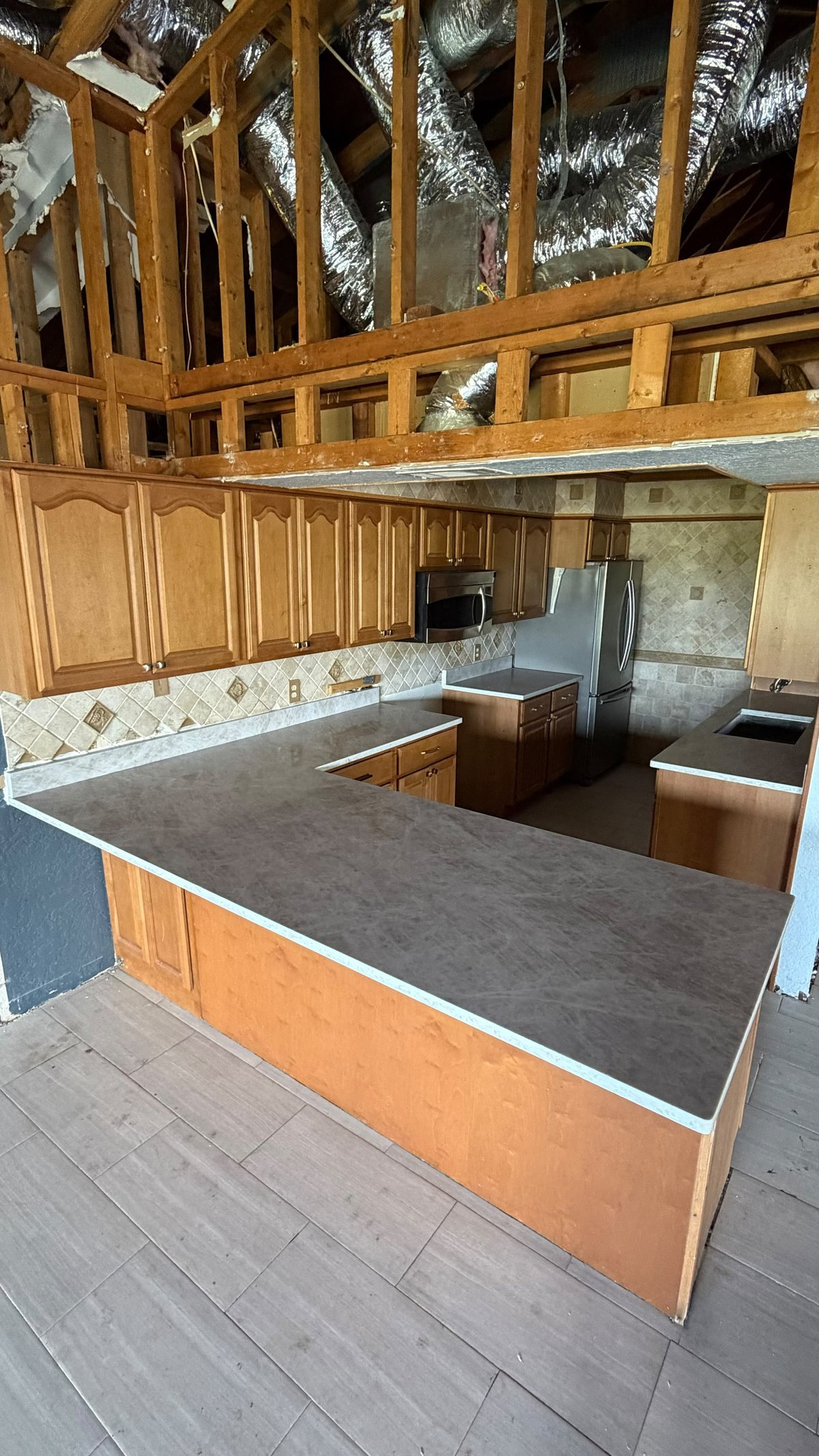 Unfinished wooden kitchen interior with exposed framing, dark countertops, cabinetry, and stainless steel appliances under construction