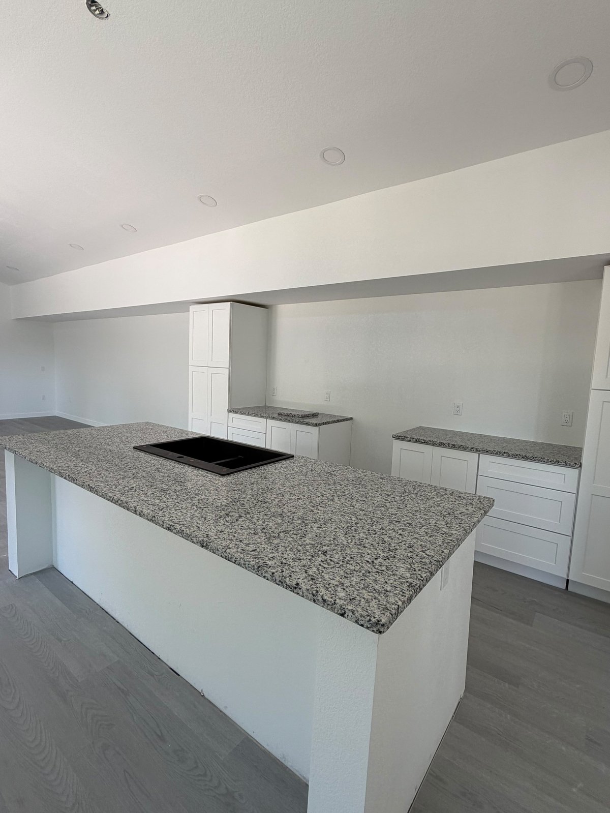 Modern kitchen with white cabinetry, granite countertops, island with cooktop, and angled ceiling with recessed lighting
