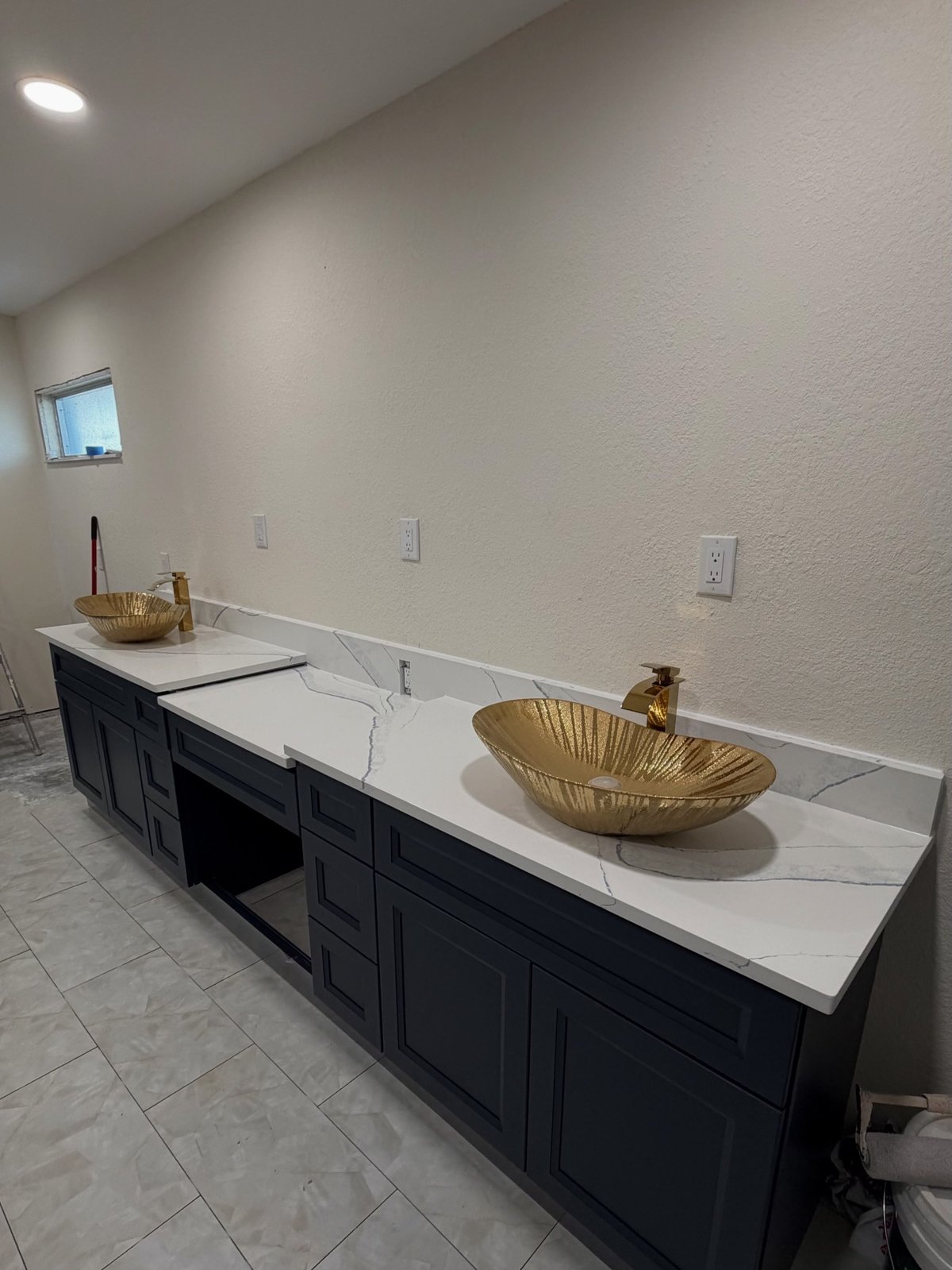 Modern bathroom vanity with black cabinetry, white marble countertop, and two gold vessel sinks in a bright white room