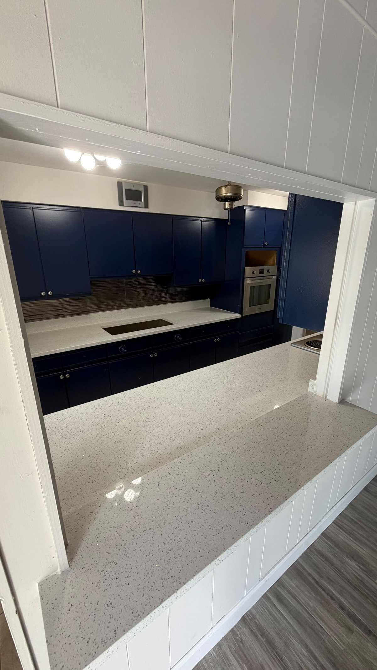Modern kitchen with dark blue cabinetry, white quartz countertops, built-in oven, and wood flooring viewed from above