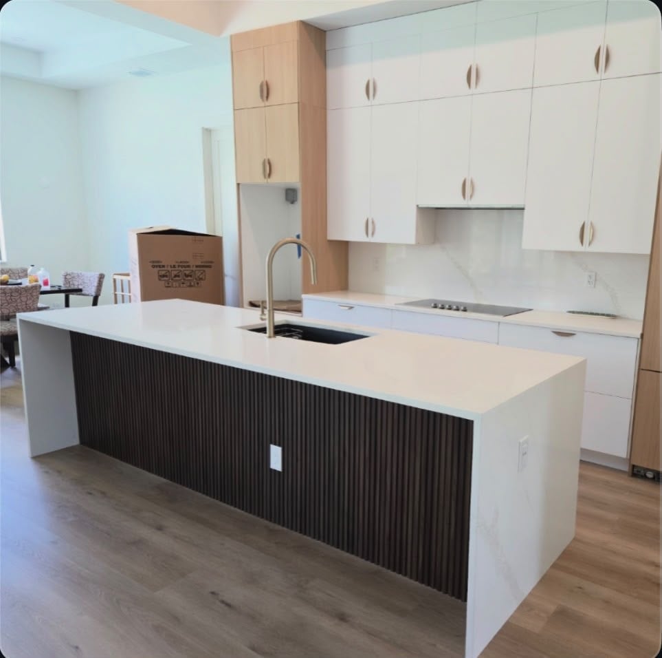 Modern kitchen with white cabinetry, large island with black ribbed panel, undermount sink, and wooden flooring