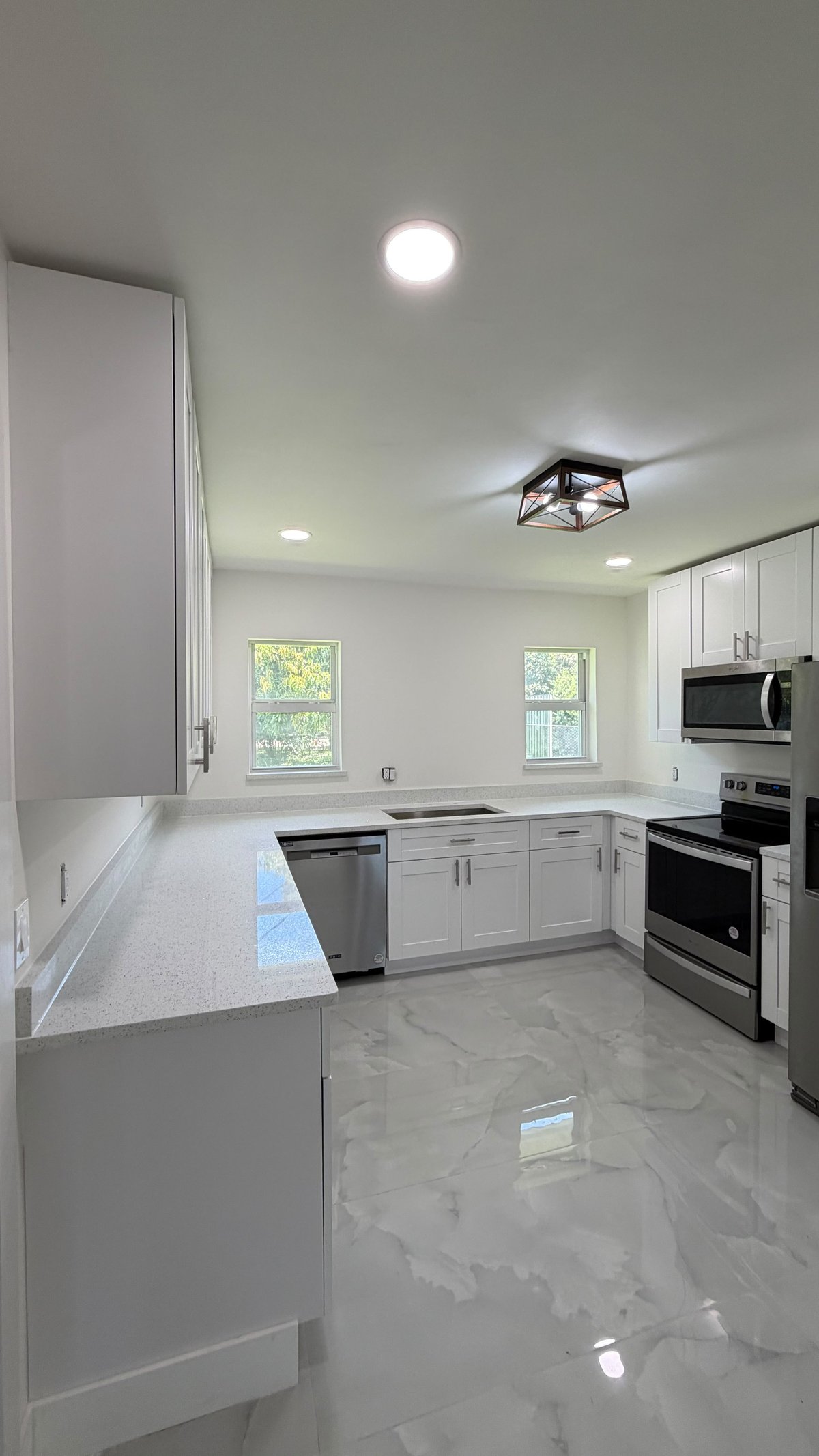 Modern white kitchen with marble floors, stainless steel appliances, white cabinetry, and natural light from two windows