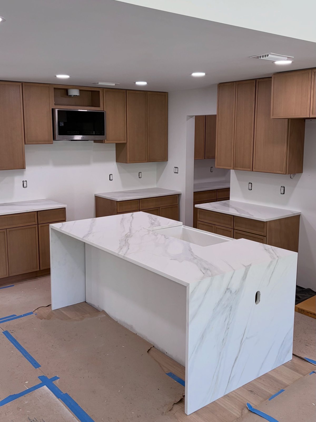 Modern kitchen under construction with white marble island, wood cabinetry, and gray ceiling with recessed lighting