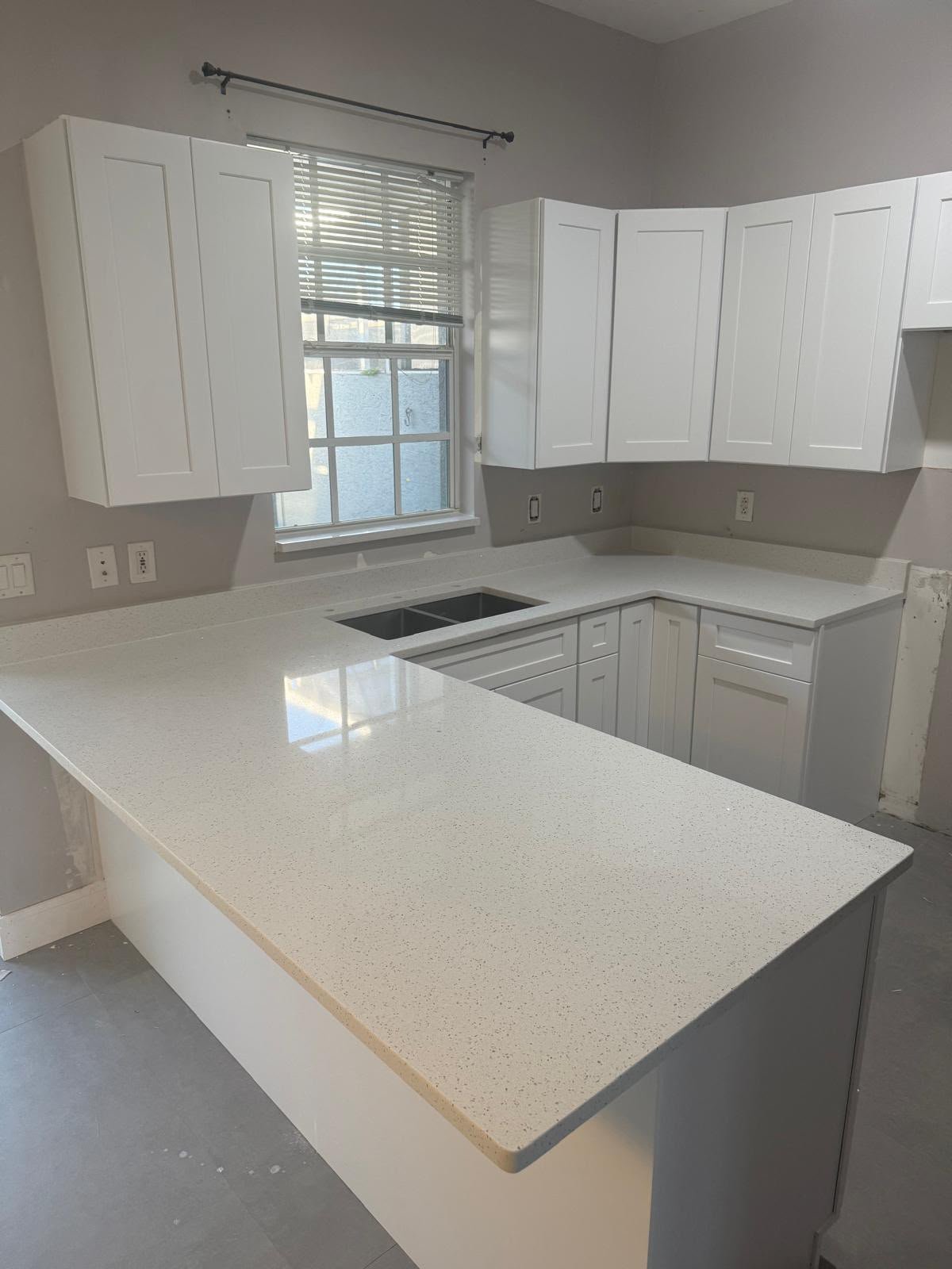 Modern kitchen with white cabinets, gray lower walls, quartz countertops, island, and window with blinds