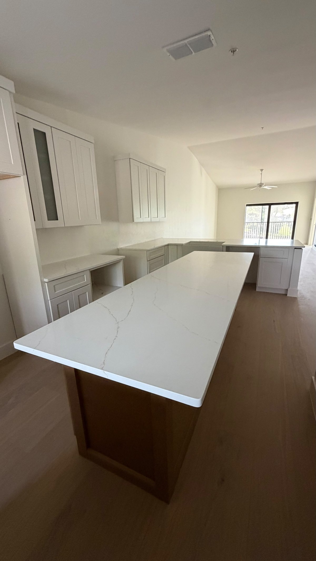 Modern kitchen interior with white quartz island countertop, gray cabinetry, and wood flooring under construction