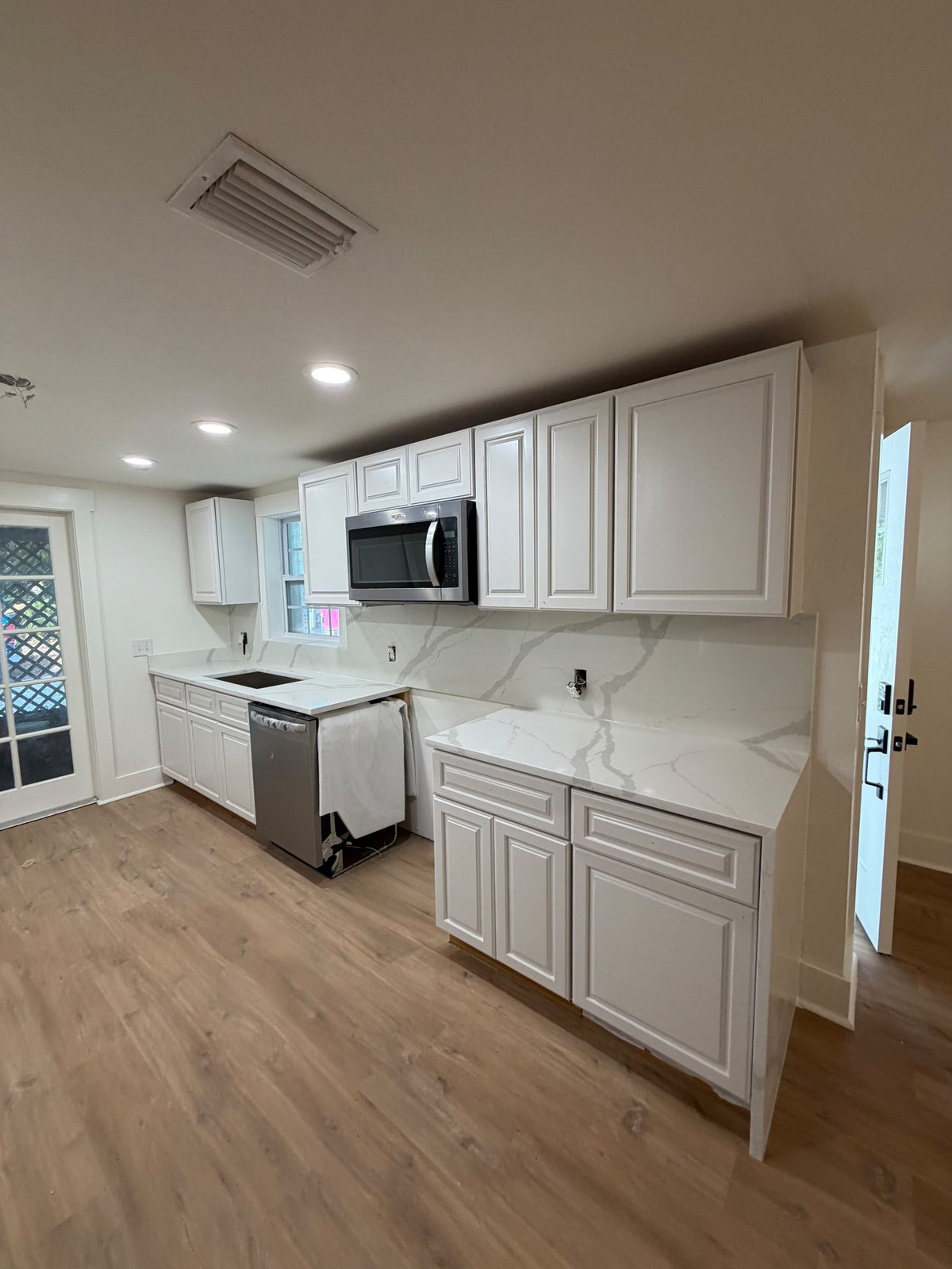 Modern kitchen with white cabinetry, marble countertops, stainless steel microwave, and wood-look flooring