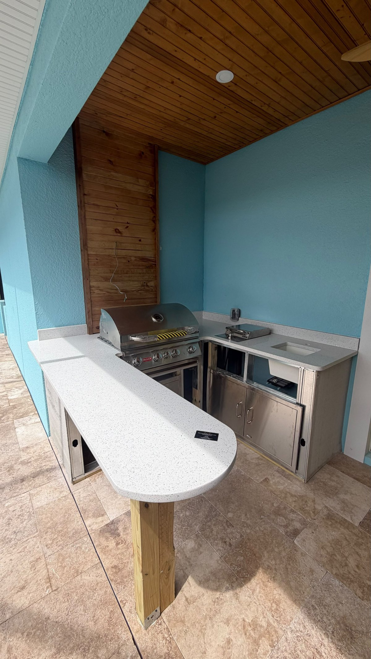 Modern kitchen with turquoise walls, wooden ceiling, and stainless steel appliances including a grill and white quartz countertops