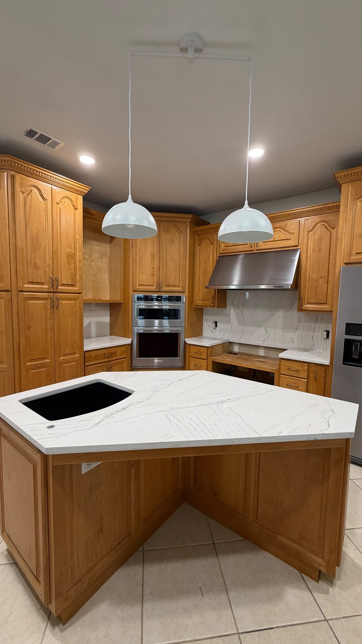Modern kitchen with wooden cabinetry, white marble island with cooktop, stainless steel appliances, and white pendant lights