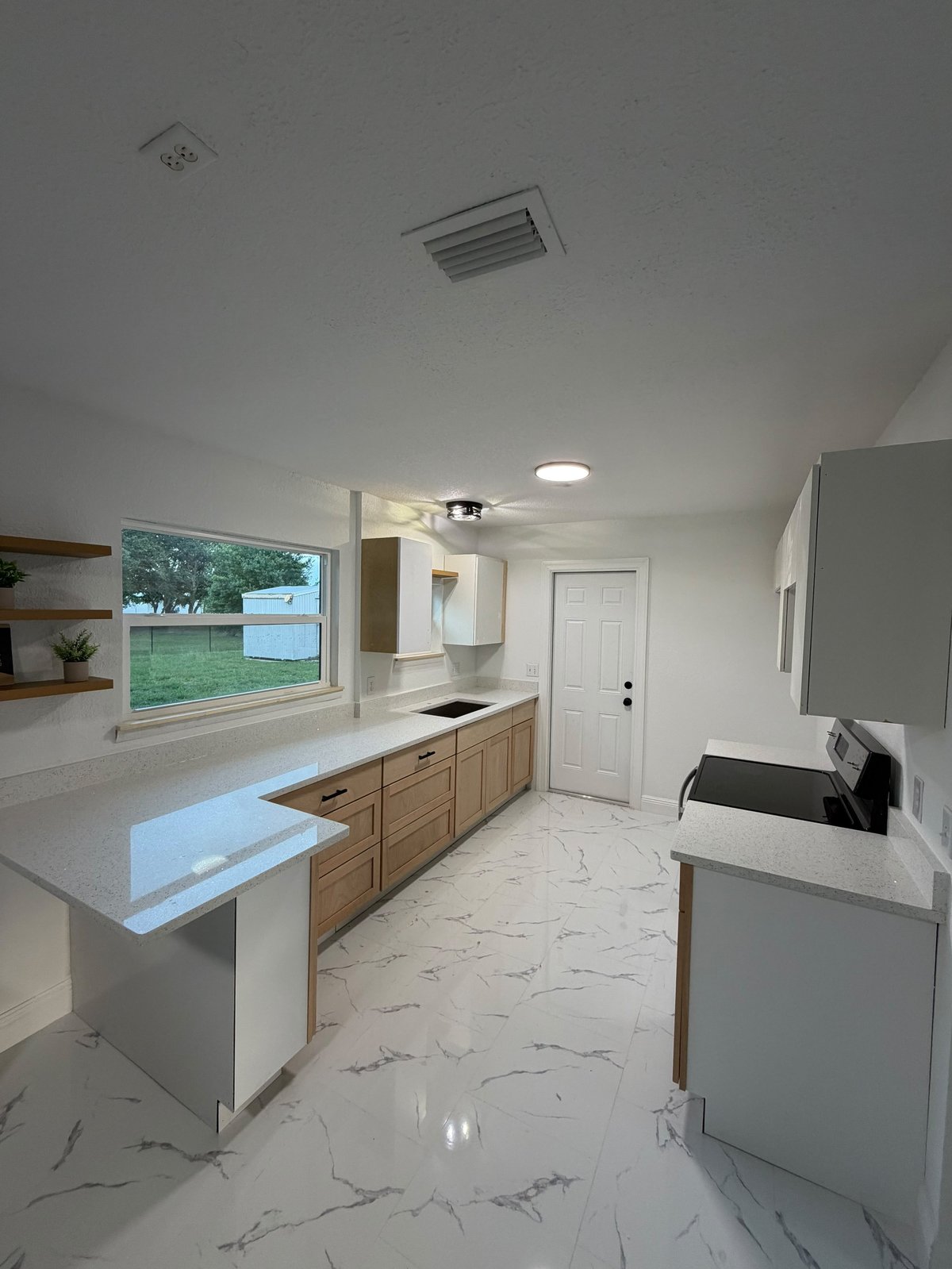 Modern kitchen with white marble flooring, wood cabinetry, white quartz countertops, and large window overlooking outdoor area